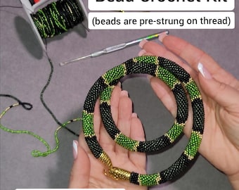 May include: A bead crochet kit with the text "Bead Crochet Kit" and "(beads are pre-strung on thread)". The kit includes a completed necklace in black and green beads, a crochet hook, and spools of thread. The necklace is held by hands.