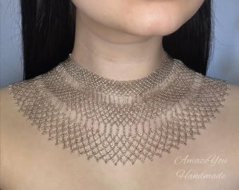 May include: A beaded necklace with a collar design. The necklace is made of small, light brown beads, creating a delicate, open-weave pattern. The text "Amaze You Handmade" is visible.