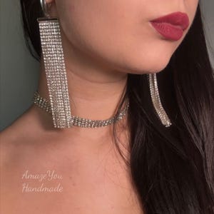 May include: A close-up of a silver rhinestone necklace and matching earrings. The earrings are long, rectangular, and dangle. The necklace is a choker style. The text "Amaze You Handmade" is visible in the bottom left corner.