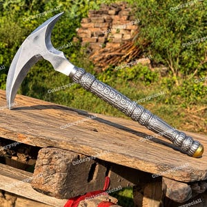 May include: A silver-toned metal war hammer featuring a curved, pointed blade head and a long, cylindrical handle decorated with intricate embossed scrollwork and textured bands, finished with a small, smooth brass-colored cap at the base.