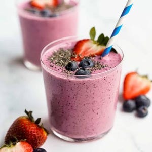 May include: Two glasses of a vibrant pink smoothie, garnished with fresh strawberries, blueberries, and chia seeds. One glass has a blue and white striped straw. The image showcases a refreshing beverage, perfect for a healthy treat.