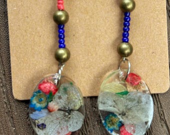Exquisite. Dangle earrings made with real pressed flowers set in clear resin, with coordinating blue and orange beads.