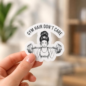 A hand holding a black and white illustration sticker of a woman with her hair in a bun lifting a barbell. This detailed view shows the artistic style of the powerlifting decals for women and the precision of the die-cut edges.