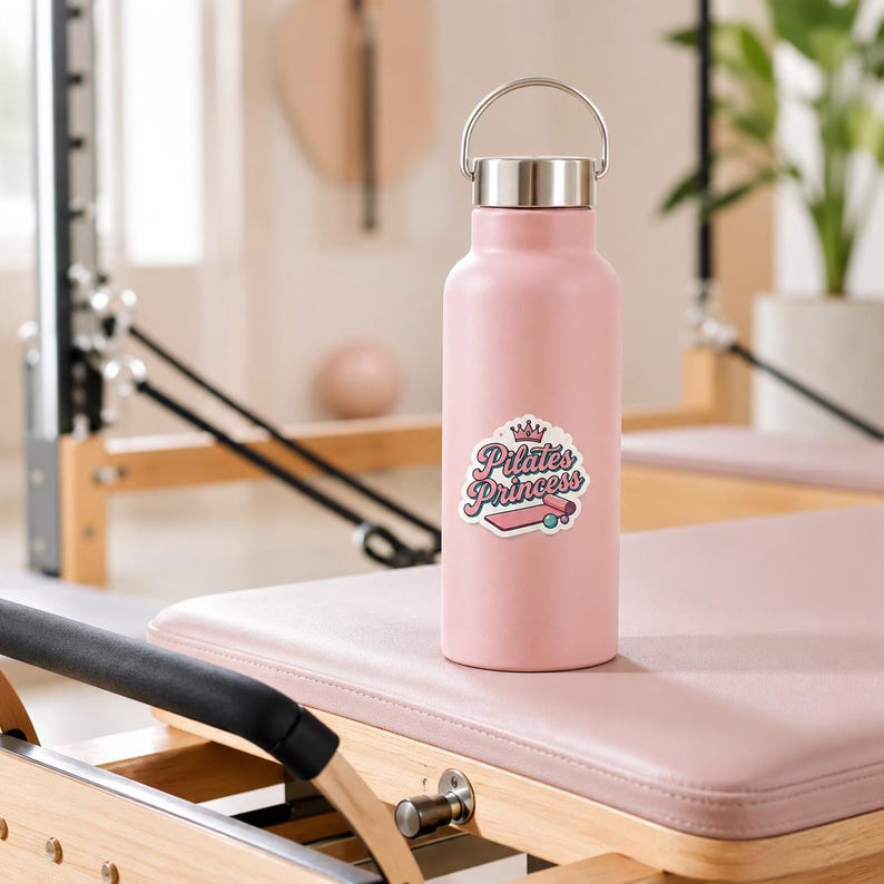 A pink water bottle decorated with a Pilates Princess sticker featuring a crown and a reformer. This lifestyle shot demonstrates how our waterproof sticker pack can beautifully personalize your daily hydration essentials.