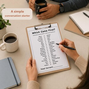 A top-down view of a person holding a clipboard with a 'Which Came First?' trivia game, surrounded by coffee mugs, notebooks, and a small plant on a neutral-toned table. This Trivia Icebreaker Game is an ideal tool for a casual meet and greet or team session.