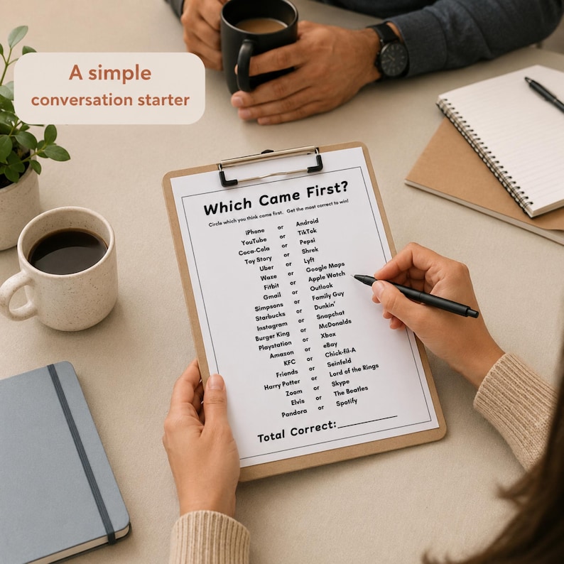 A top-down view of a person holding a clipboard with a 'Which Came First?' trivia game, surrounded by coffee mugs, notebooks, and a small plant on a neutral-toned table. This Trivia Icebreaker Game is an ideal tool for a casual meet and greet or team session.