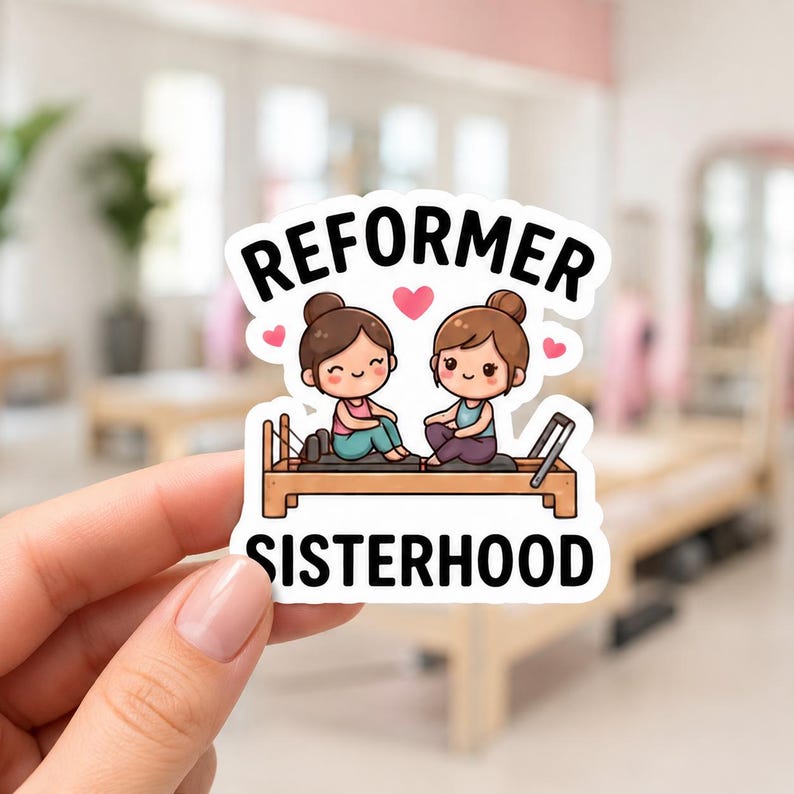 A hand holding a white sticker featuring a cartoon illustration of two girls sitting on a Pilates reformer machine. This funny reformer stickers design is a charming addition to any pilates princess kit or fitness enthusiast's collection.