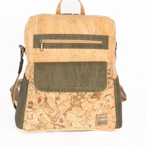 May include: A tan and green cork backpack. It features a top handle, a zipped front pocket, and a flap pocket. The shoulder straps and back are green. The bag has a small logo on the bottom right. Measurements are in centimetres.