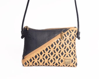 May include: A crossbody bag featuring a diagonal design with a dark charcoal section and a tan cork section with a black geometric diamond pattern. It includes a diagonal zipper, a thin shoulder strap, and a small rectangular label reading CorkRoots.