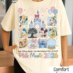 May include: Ivory-colored t-shirt featuring Disney characters like Mickey Mouse, Minnie Mouse, and Goofy. The shirt includes the text "Walt Disney World, Pixie Magic 2026" and "Comfort Ivory". The design includes a castle and balloons.