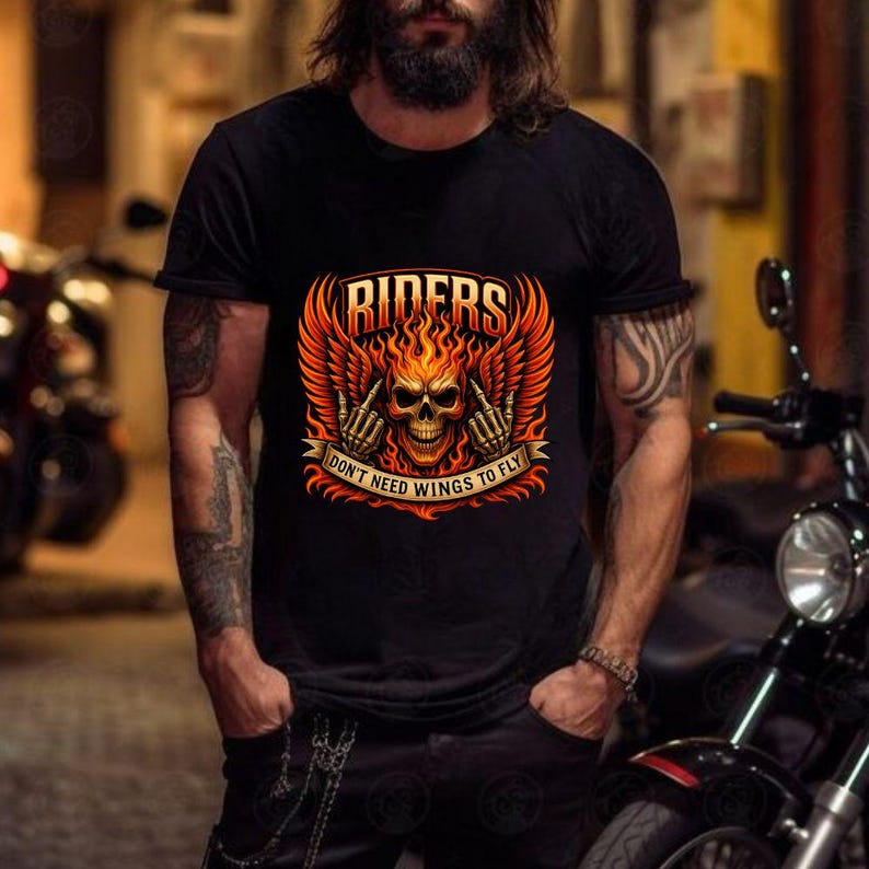 K&ouml;nnte beinhalten: Schwarzes T-Shirt mit einem flammenden Totenkopf-Design, dem Wort "RIDERS" dar&uuml;ber und dem Text "DON'T NEED WINGS TO FLY" darunter. Das Design beinhaltet orangefarbene und rote Fl&uuml;gel und Flammen. Das T-Shirt wird von einer Person getragen.