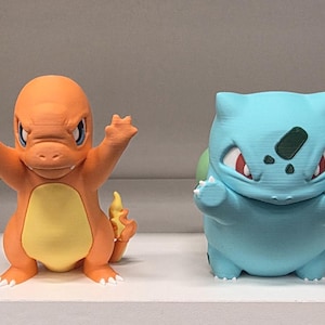 Puede incluir: Un conjunto de cuatro figuras de personajes Pokémon alineadas. De izquierda a derecha, un Pikachu amarillo, un Charmander naranja, un Bulbasaur azul claro y un Squirtle azul claro. Cada figura está posada con los brazos extendidos en una postura dinámica.
