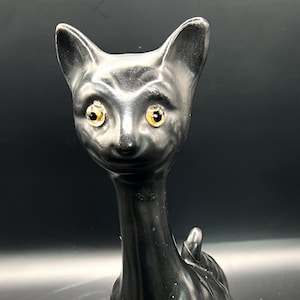 May include: A black cat figurine with a long neck and golden eyes. The cat is sitting with its front paws forward and its tail curled up. The figurine has a glossy finish.