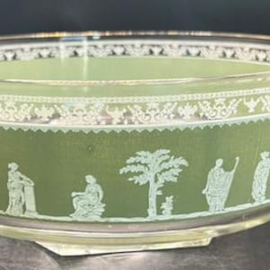 May include: A clear glass bowl with a wide, shallow design. The bowl features a green band with white classical figures and decorative patterns. The bowl's rim and base are clear, and the overall aesthetic is vintage.