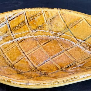 May include: An oval ceramic serving dish with a textured, grid pattern in yellow and brown, with white highlights. The rim has a rope-like design. A decorative piece for the kitchen. The dish measures approximately 30 cm in length.