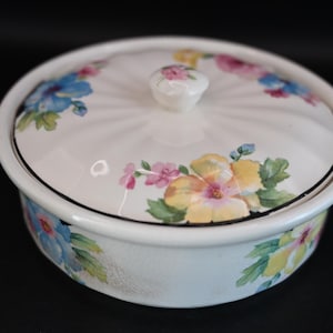 Könnte beinhalten: Eine weiße Keramikschale mit Deckel, verziert mit einem Blumendesign mit blauen, gelben, rosa und grünen Blumen. Der Deckel hat einen Knopf in der Mitte.