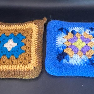 May include: Two handmade crochet potholders. One is brown with a blue and white center, the other is blue with a multicolored center. Both are square with a small loop for hanging. These potholders are perfect for kitchen use.