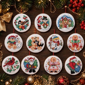 May include: Twelve round, embroidered Christmas decorations, each with a unique festive design. The ornaments depict scenes such as a bird, snowman, Santa Claus, a house, teddy bears, and gingerbread people. They are white with red hanging ribbons.