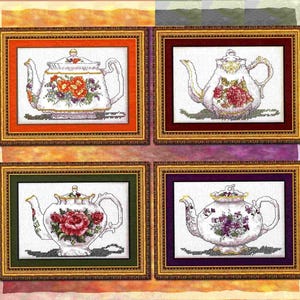 Könnte beinhalten: Vier gerahmte Kreuzstich-Kunstwerke mit weißen Teekannen, die mit floralen Designs verziert sind. Jede Teekanne hat ein anderes Farbschema, darunter orange, rote, rosa und lila Blumen. Die Rahmen haben verzierte goldene und farbige Ränder.