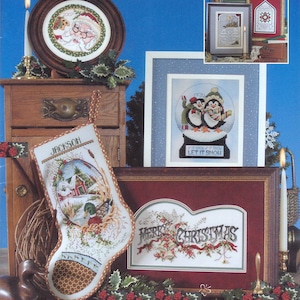 May include: A selection of framed cross-stitch art and a Christmas stocking. The art features a snow globe with penguins, a festive scene, and a framed piece with "Merry Christmas." The stocking is personalised with the name "Jackson."