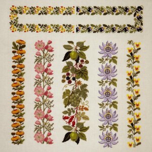 Op de afbeelding: Kruissteek borduurwerk sampler met bloemen en botanische ontwerpen. De sampler bevat randen en verticale patronen van verschillende bloemen, vruchten en bladeren in tinten geel, roze, paars, groen en bruin, allemaal tegen een witte achtergrond.