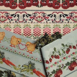 May include: Cross-stitch patterns featuring various designs. The top row has smiling red tomatoes. Below are cows with hearts, pink pineapples, and chicks with a heart. The bottom rows show carrots, strawberries, and floral patterns. The color palette includes red, pink, green, and blue.