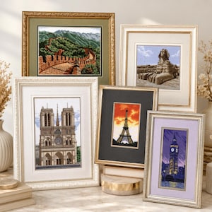 May include: A collection of framed cross-stitch artworks featuring iconic landmarks. The images include the Great Wall of China, the Sphinx, Notre Dame Cathedral, the Eiffel Tower, and Big Ben. Each piece is framed in a decorative style.