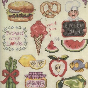 May include: Cross-stitch sampler featuring various food items. Includes a hamburger, pretzel, ice cream cone, watermelon slice, asparagus tied with a red bow, lemon, apple, fish, pear, and a jar of jam. The words "Baked with Love" and "Kitchen Open" are also present.