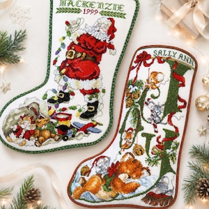 Puede incluir: Dos calcetines navideños con diseños bordados. Uno presenta a Papá Noel con el nombre "MacKenzie" y el año "1999". El otro tiene el nombre "Sally Ann" con una gran letra "J" e imágenes festivas, incluyendo ratones y un oso de peluche.