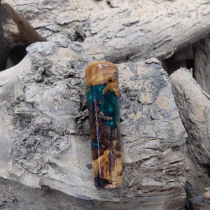 Pode incluir: Uma caneta de madeira e resina verde com um padrão de espiral único. A caneta tem aproximadamente 10 cm de comprimento e tem uma ponta arredondada.