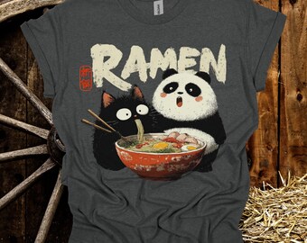 May include: Dark gray t-shirt featuring a cartoon illustration of a black cat and a panda bear sharing a bowl of ramen. The word "RAMEN" is printed in large, white letters above the image. The shirt is made of a soft material.