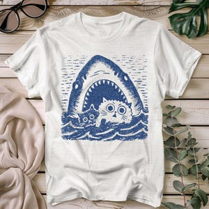 Camiseta divertida con un gato y un tiburón: adorables gatos de dibujos animados escapando de un tiburón gigante. Perfecta para amantes de los gatos y del humor. Un regalo gráfico único.