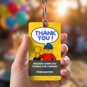 Può includere: Un'etichetta regalo rettangolare gialla con un cordino color arcobaleno. L'etichetta presenta un personaggio dei cartoni animati con una maglietta rossa e un berretto blu che tiene un trofeo d'oro, con un fumetto THANK YOU! e il testo MISSION COMPLETE! THANKS FOR COMING! FROM MATHEO.