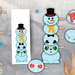 Op de afbeelding: Een winterthema knutselproject met sneeuwman uitsparingen en accessoires zoals hoeden, sjaals en wanten. De uitsparingen zijn bevestigd aan wasknijpers, wat duidt op een doe-het-zelf activiteit voor kinderen of feestelijke decoraties.