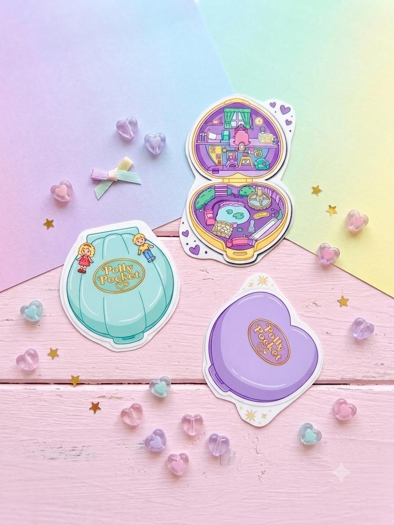 May include: Three Polly Pocket stickers featuring a teal shell-shaped case with two figures, an open heart-shaped case revealing a detailed interior room and garden scene, and a closed purple heart-shaped case, all decorated with small heart accents.
