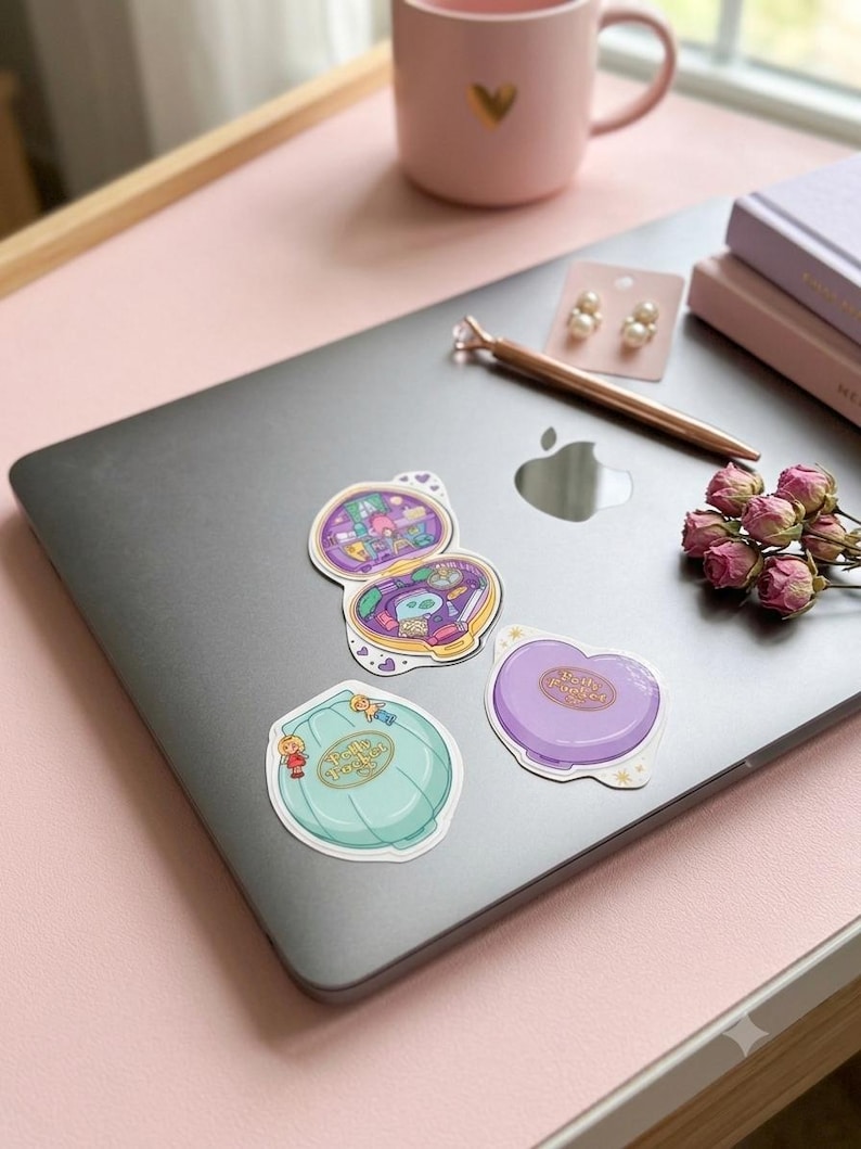 May include: Three vinyl stickers featuring Polly Pocket designs. One sticker shows an open compact with a detailed interior, while the other two depict closed compacts in light blue and purple, each labeled with the Polly Pocket brand name.