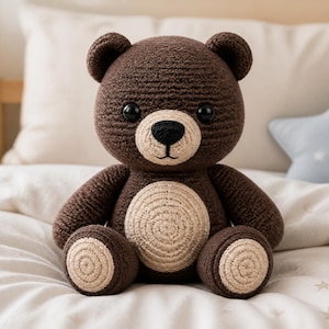 Könnte beinhalten: Ein handgefertigter brauner Häkelteddybär mit beigem Bauch und Pfoten. Der Bär hat schwarze Sicherheitsaugen und eine schwarze Nase. Er sitzt auf einer weißen Tagesdecke. Der Bär ist ein weiches Spielzeug.