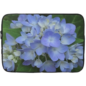 May include: Laptop sleeve featuring a close-up of a hydrangea flower. The image showcases a cluster of blue and white petals with green leaves in the background. The sleeve has a black border.