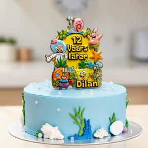 Pode incluir: Um bolo azul-claro decorado com pérolas brancas, algas verdes e conchas brancas. Um topo de bolo colorido com o tema Bob Esponja apresenta o texto 12 Years later e Dilan, rodeado por personagens de desenhos animados.