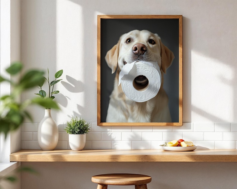 May include: A framed print featuring a golden Labrador Retriever holding a roll of white toilet paper in its mouth. The dog is centered in the frame, with a neutral background. The wooden frame adds a classic touch to the artwork.