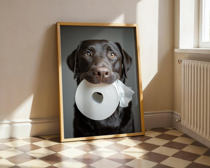 Puede incluir: Impresi&oacute;n enmarcada de un Labrador Retriever color chocolate sosteniendo un rollo de papel higi&eacute;nico blanco en la boca. El perro tiene ojos marrones y pelaje marr&oacute;n oscuro. El marco es de madera clara y el fondo gris neutro.