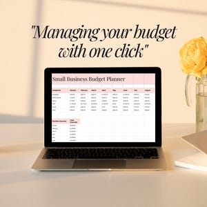 May include: A laptop displaying a small business budget planner spreadsheet. The screen is open on a white desk, next to a glass candle holder, a notebook, and a vase of yellow flowers. The text "Managing your budget with one click" is above the laptop.