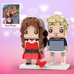 May include: A Lego-style figurine set of a couple, with a photo insert labelled "Your Photo." The figures are constructed from colourful blocks, the woman in a red dress and the man in a striped shirt. A red heart is positioned between them.