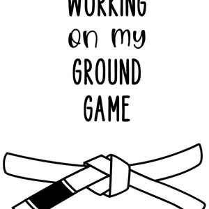 Może przedstawiać: Biała grafika z napisem "WORKING on my GROUND GAME" w czarnym kolorze. Poniżej biało-czarny pas do sztuk walki, zawiązany na środku. Obraz na białym tle.