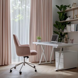 May include: A modern home office setup featuring a white desk with a laptop, a pink upholstered office chair, and a white filing cabinet. The room has pink curtains and a shelf with plants and books.