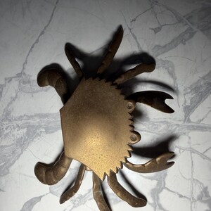May include: A brass crab-shaped decorative object. The crab has a central body with a textured surface and a jagged edge. It features multiple legs and claws, all in a brass finish. The object is designed to resemble a crab.