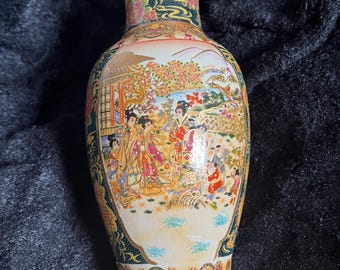May include: A white porcelain vase with a gold and black floral design. The vase features a scene of Japanese women in traditional clothing.