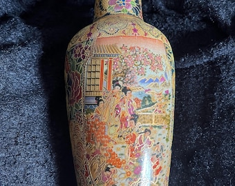 May include: A tall, ceramic vase with a gold and white background. The vase is decorated with a colourful floral pattern and a scene of people in a garden. The vase has a narrow neck and a wide base.