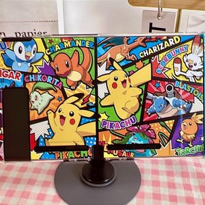 Könnte beinhalten: Eine Nintendo Switch-Konsole mit einem individuellen Skin mit Pokémon-Charakteren wie Pikachu und Charizard. Die Joy-Cons sind rot und blau. Das Design ist farbenfroh und auffällig.