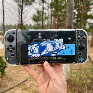 Könnte beinhalten: Eine transparente Schutzhülle für eine Nintendo Switch-Konsole. Die Hülle zeigt eine blau-weiße Grafik im Anime-Stil eines Charakters. Blaue Pluszeichen und andere blaue Akzente verzieren die Hülle.